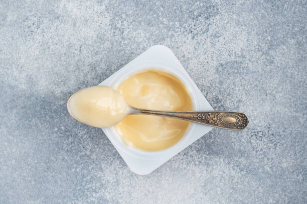 istock Milk fruit yogurt in an open package and a teaspoon. Gray concrete background, copy space. 1299388418