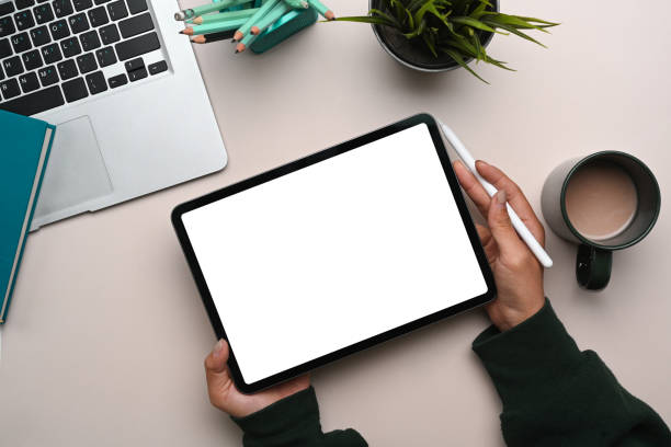 istock Top view of young woman hands holding mock up digital tablet on her workspace. Blank screen for advertise text. 1299389391