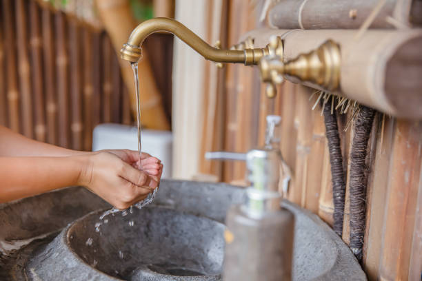 Close up shot of an unrecognizable Asian woman washing her hands in a restaurant. A clean water flowing from the faucet into the woman hand. The background is a bamboo wall and the basin is from terrazzo