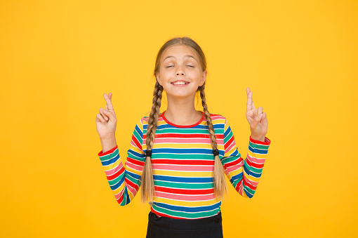 I dont want to jinx it. Cute child make wish yellow background. Little child keep fingers crossed for luck. Small child with long hair braids in casual fashion. Her child dream.