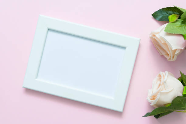 istock Blank white frame mockup with pastel roses on pink backgroud for love, wedding or valentine day theme 1299391898