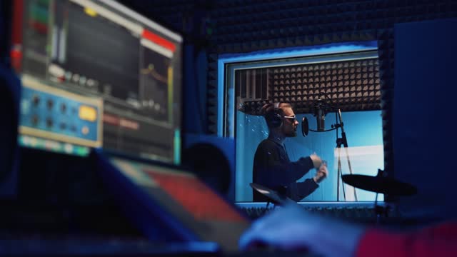 Male Rap Singer with Headphones and Sound Engineer are recording a new song