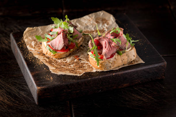 istock Bruschetta with roast beef and arugula on a wooden board 1299400635