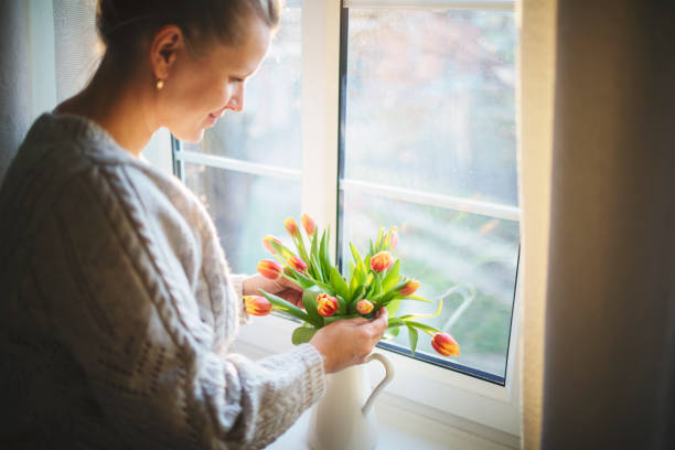 Pretty woman with fresh tulips by the window .