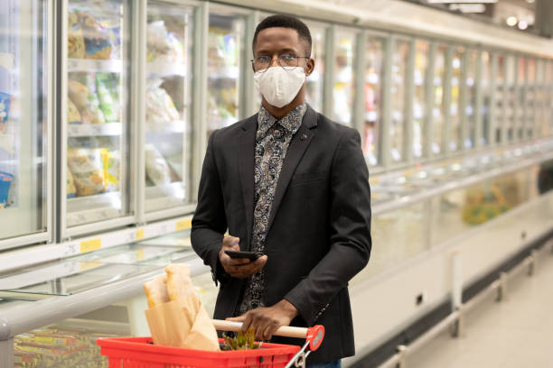 istock Young elegant African businessman using smartphone while shopping in supermarket 1299406616