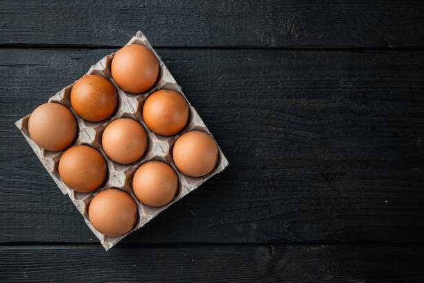 istock Brown eggs in carton box tray, on black wooden table background, top view flat lay , with space for text  copyspace 1299407971