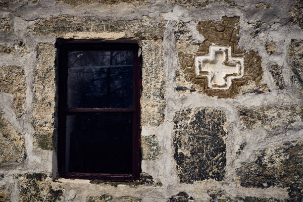 Close-up of an exterior stone wall of an old church with a window and cross, Bulgaria