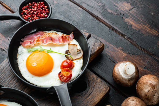 istock Scrambled eggs in frying pan with pork lard, bread and green feathers in cast iron frying pan, on old dark  wooden table background , with space for text  copyspace 1299409708