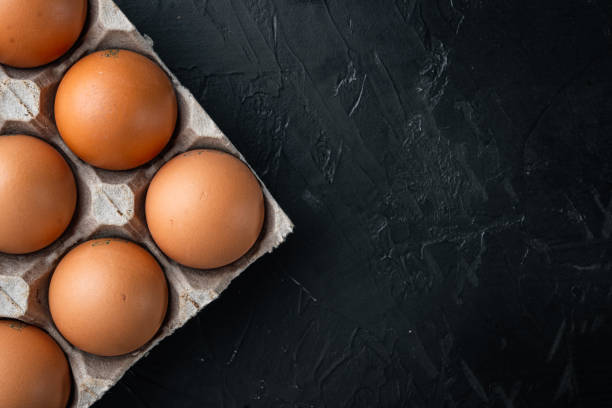 istock Brown eggs in carton box tray, on black background, top view flat lay , with space for text  copyspace 1299409784