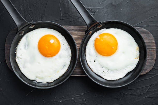 istock Fried eggs with cherry tomatoe and bread for breakfast in cast iron frying pan, on black background, top view flat lay 1299410809