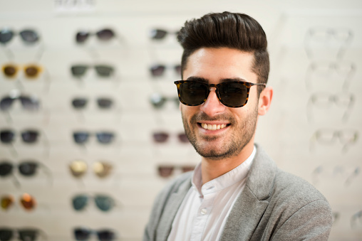 Man looking some glasses in optical store, trying on lenses and looking at camera with sunglasses