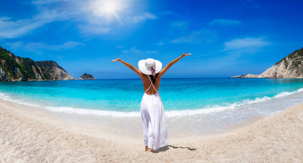 una donna in abito bianco e cappello gode della bellissima spiaggia di petani, cefalonia, grecia - sea swimming greece women foto e immagini stock