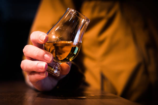 Close up shot a Glencairn whisky glass Color close up shot a hand holding a Glencairn whisky glass on a wooden table, with shallow depth of field. tasting stock pictures, royalty-free photos & images