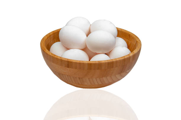 istock White raw eggs lie in a wooden bowl on a white isolated background. Side view. 1299418444