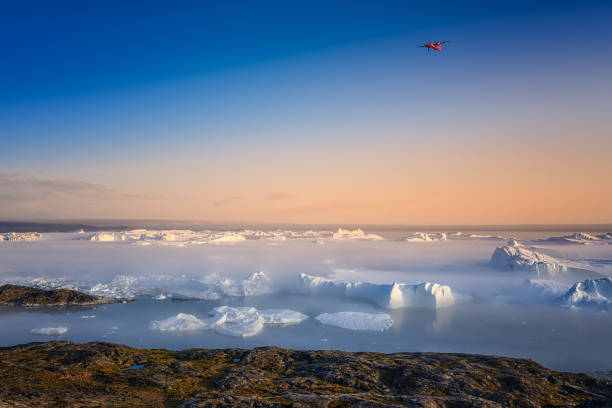 large glaciers in the bay by the rocky shore in the light of the setting sun with fog over the water with orange tourist tent