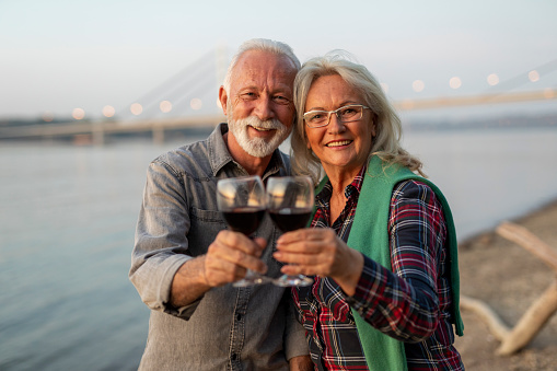 Smiling senior couple drinking wine at the riverside.