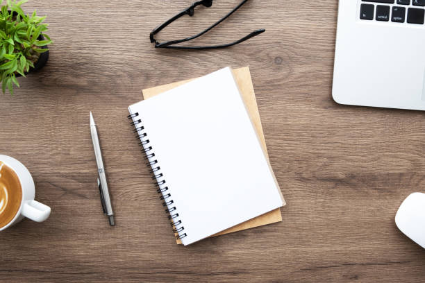 istock Blank notebook with pen are on top of wood office desk table with laptop computer, and supplies. Top view with copy space. Morning life working from home concept. 1299443106