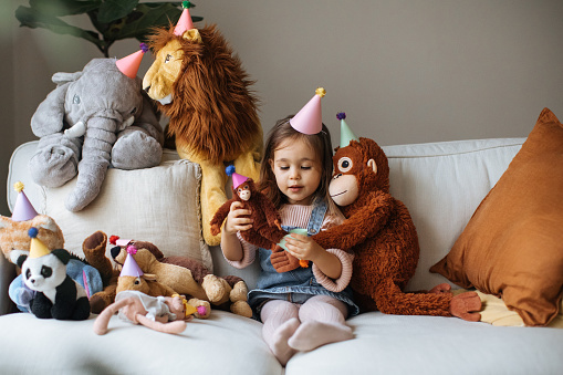 Cute happy little girl embracing teddy bear. Pretty female kid at home, sitting on sofa with her favorite toy, copy space