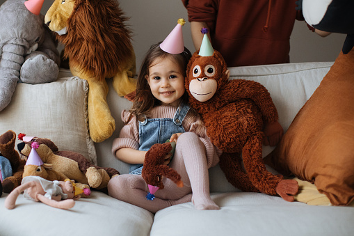 Cute happy little girl embracing teddy bear. Pretty female kid at home, sitting on sofa with her favorite toy, copy space
