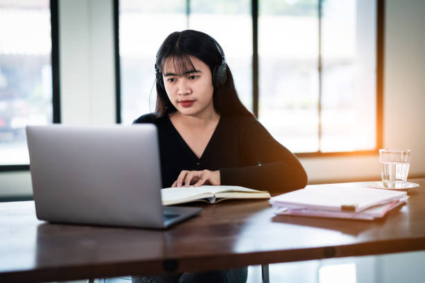 istock Teenage university student wears wireless headphones write on the notebook to study language online watch and listen to the lecturer, webinar via video call e-learning at home, distance education 1299445778