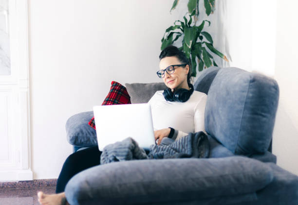 istock woman with her laptop working from her couch at home using headphones 1299447230