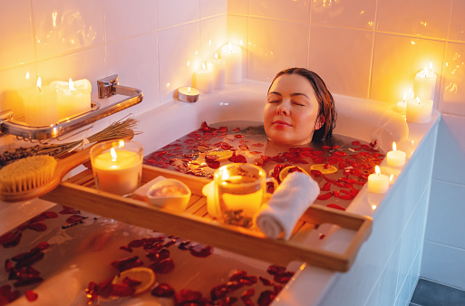 Mujer joven disfrutando de aura espiritual limpieza baño de flores de rosa con pétalos de rosa y velas durante el ritual de luna llena. Cuidado del cuerpo y rutina de salud mental. photo