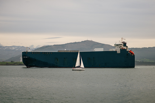 A small sailboat close to a large cargo ship in Santander bay, Cantabria, Spain