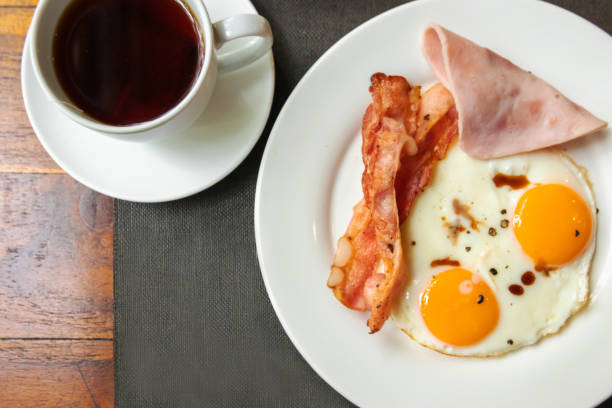istock Delicious breakfast;  sunny-side-up fried egg, ham, bacon with black coffee; top view on wooden table. 1299451770