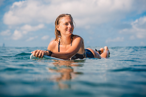 Attractive surfing woman with surfboard. Surf girl paddle on surfboard in ocean