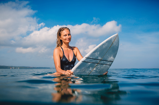 Surfer woman look at camera and sitting on the surfboard. Surfgirl with surfboard in ocean.