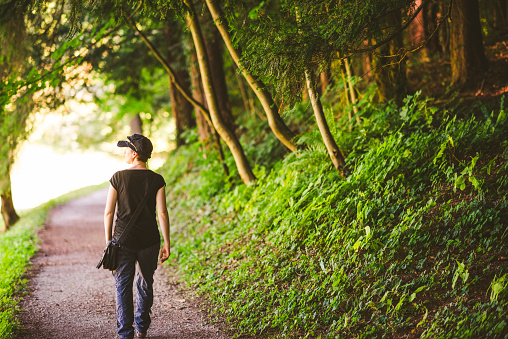 Casual dressed woman walking on a shady summer path in forest