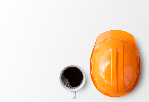 Orange safety engineer helmet and cup of coffee on white background. top view with copy space for design.
