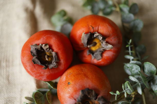 istock Three Persimmons on Burlap Fabric, Green Branches Around the Persimmons, Close-up 1299465113