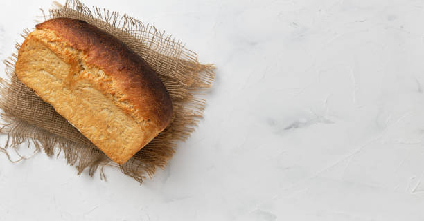 A loaf of white rustic bread on a linen lining on a white table. Small business idea, custom-made sourdough bread. Top view with copy space