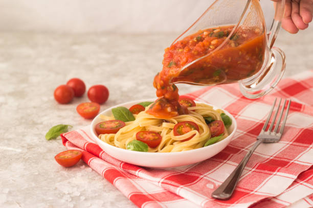 pasta marinara in a white plate on a white table with tomato wedges and basil leaves