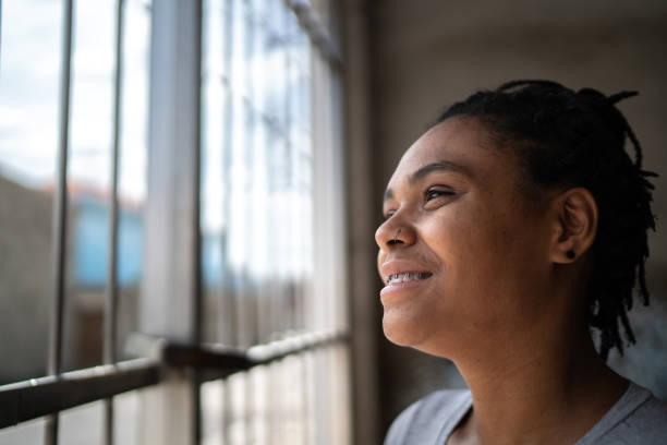 istock Young woman looking through the window at home 1299469504