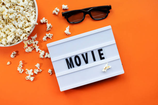 istock Popcorn, 3D glasses and lightbox text Movie time on orange paper background. Top view Template 1299470793