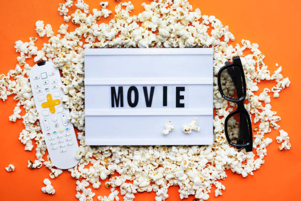 istock Popcorn, remote control, 3D glasses and lightbox text Movie time on orange paper background. Top view Template 1299471376
