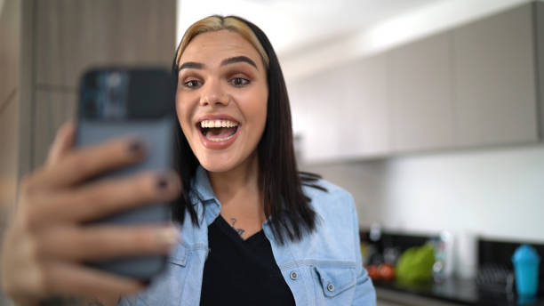 donna transgender che fa una videochiamata su smartphone a casa - solo una donna giovane foto e immagini stock