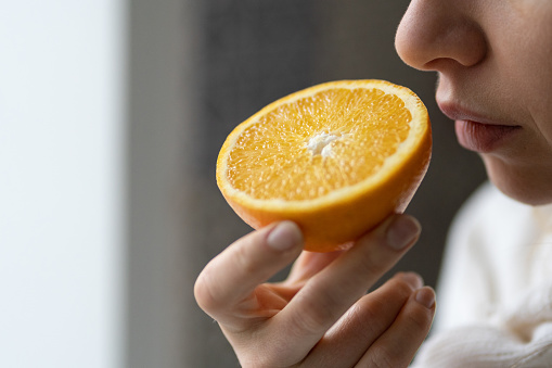 Mujer enferma tratando de sentir el olor de la mitad de la naranja fresca, tiene síntoma de Covid-19, pérdida de olor, sabor photo