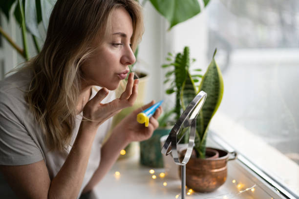 Woman applying moisturizing nourishing balm to her lips with finger to prevent dryness and chapping Woman applying moisturizing nourishing balm to her lips with her finger to prevent dryness and chapping in the cold season, sitting by the window, looking at mirror. Lip protection. herpes stock pictures, royalty-free photos & images