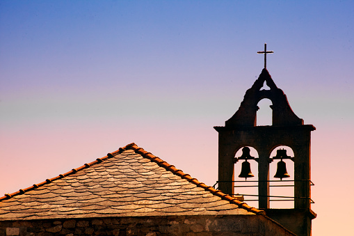 Church slate rooftop, cattail and belfry outlined, religious cross on it, sunset background. Copy space available on the left side of the image. A Coruna province, Galicia, Spain.