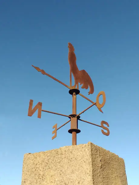 Cast iron rooster wind vane under blue sky. Weather vane to indicate the direction of the wind with a wrought iron rooster and cardinal points. Meteorology accessory concept.