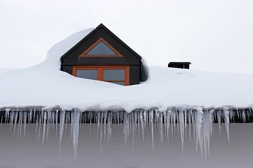 Large dangerous icicles and a roof avalanche on a house roof in winter