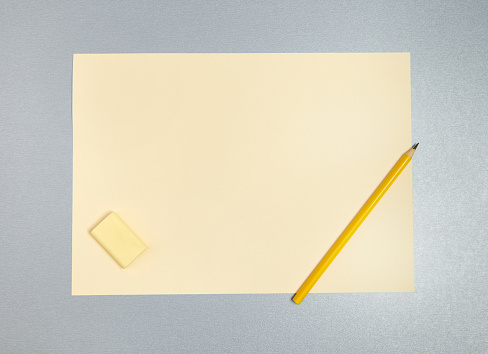 Flat lay photo of yellow eraser, pencil and sheet of paper on a gray background