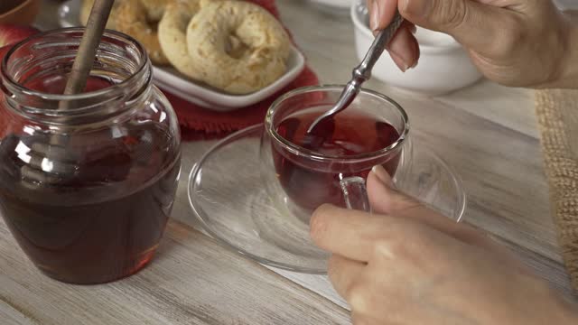 High angle close-up view of woman hands stirring a hibiscus hot tea in a cup on a white rustic table