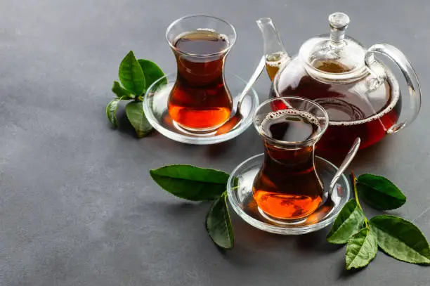 Glass cup of black tea with fresh tea leaves, traditional turkish brewed hot drink