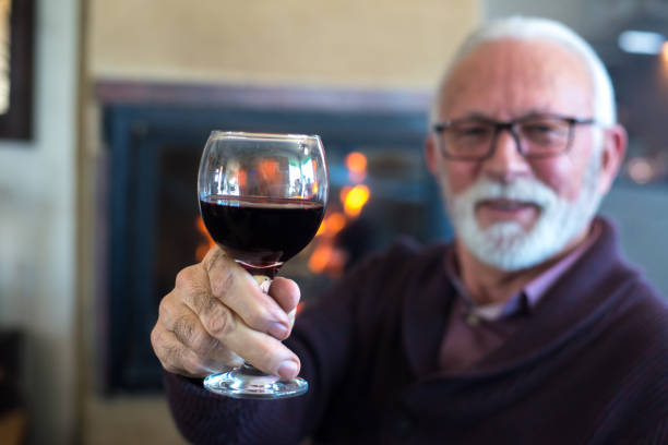 istock Senior man drinking wine in front of the fireplace 1299488194