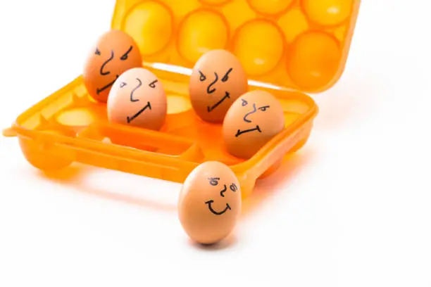 Picture of Obsolete Orange Egg Hiolder. Placed With Eggs Symbolizing Embittered Human Faces.Against White Background.Horizontal Composition