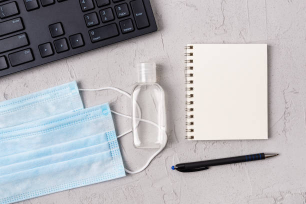 istock Copy space on spring notebook near medical face mask, hand sanitizer and PC keyboard over textured gray backgroung. Protection against covid, flu and viral infections, concept. 1299489969